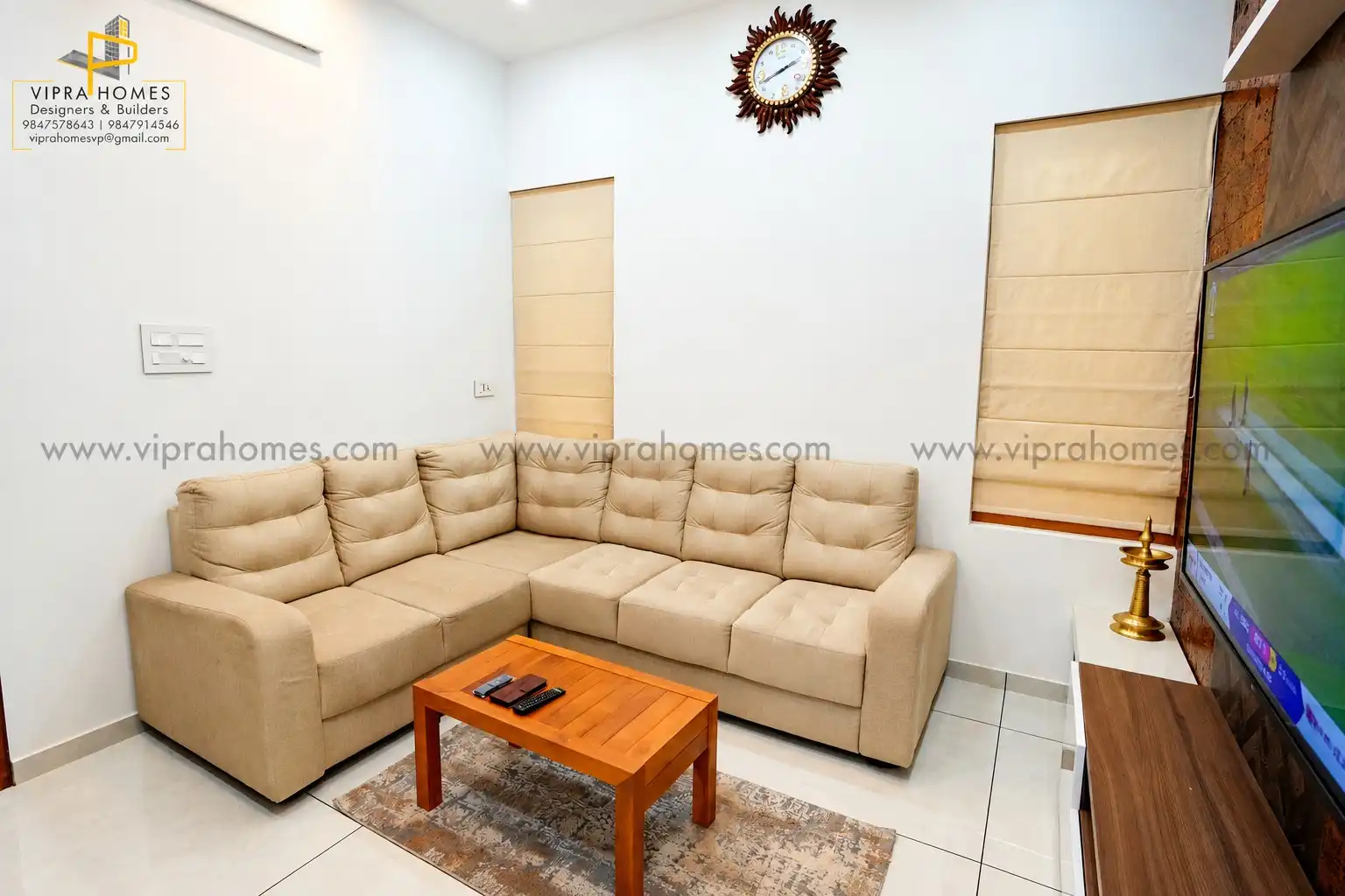 A living room by VIPRA HOMES with a beige L-shaped sofa, timber coffee table and Roman blinds