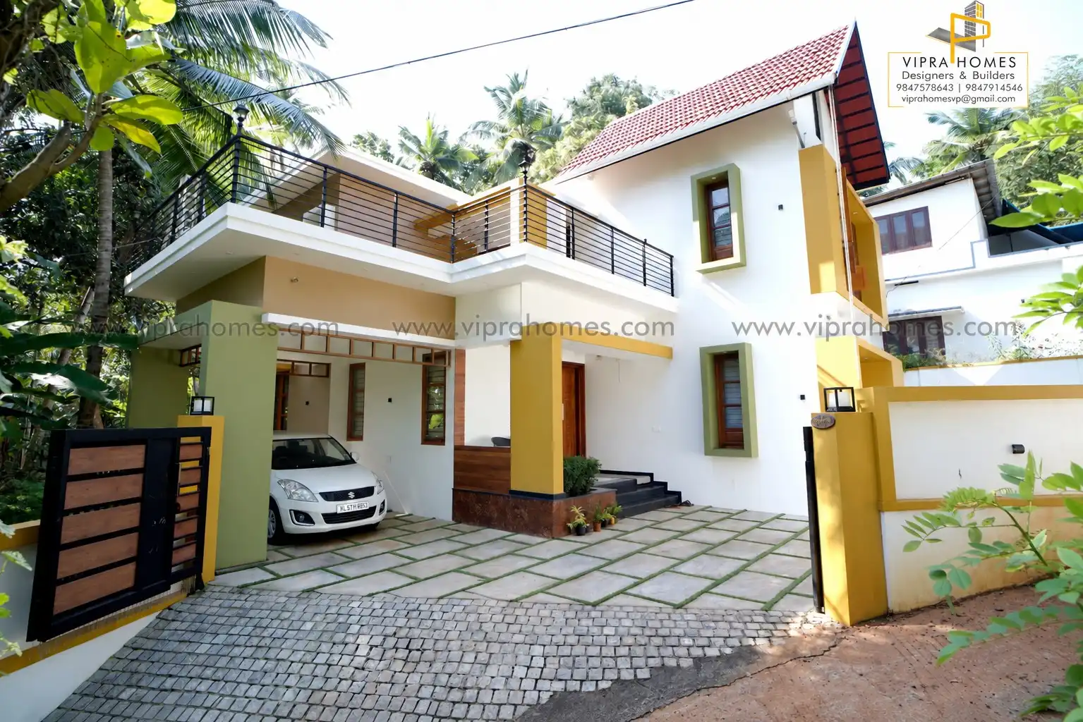 A VIPRA HOMES residence with ochre and olive accents, a car porch, balcony railings and a stone-paved courtyard