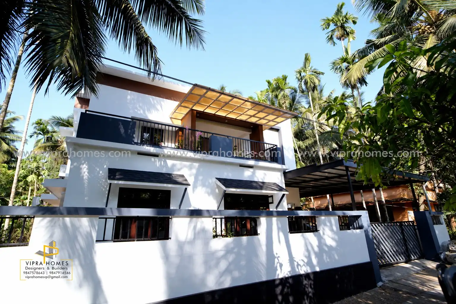 A contemporary white VIPRA HOMES residence with dark window canopies, a glazed balcony roof and palm trees
