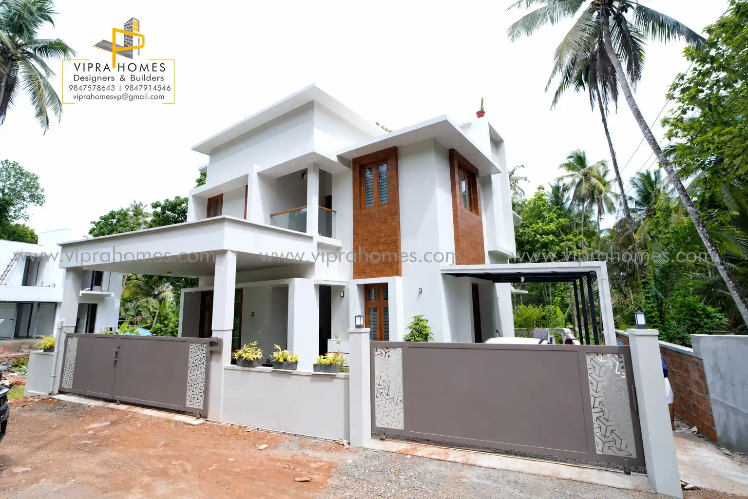 A white two-storey VIPRA HOMES residence with a laterite-brick tower, car porch and patterned gate
