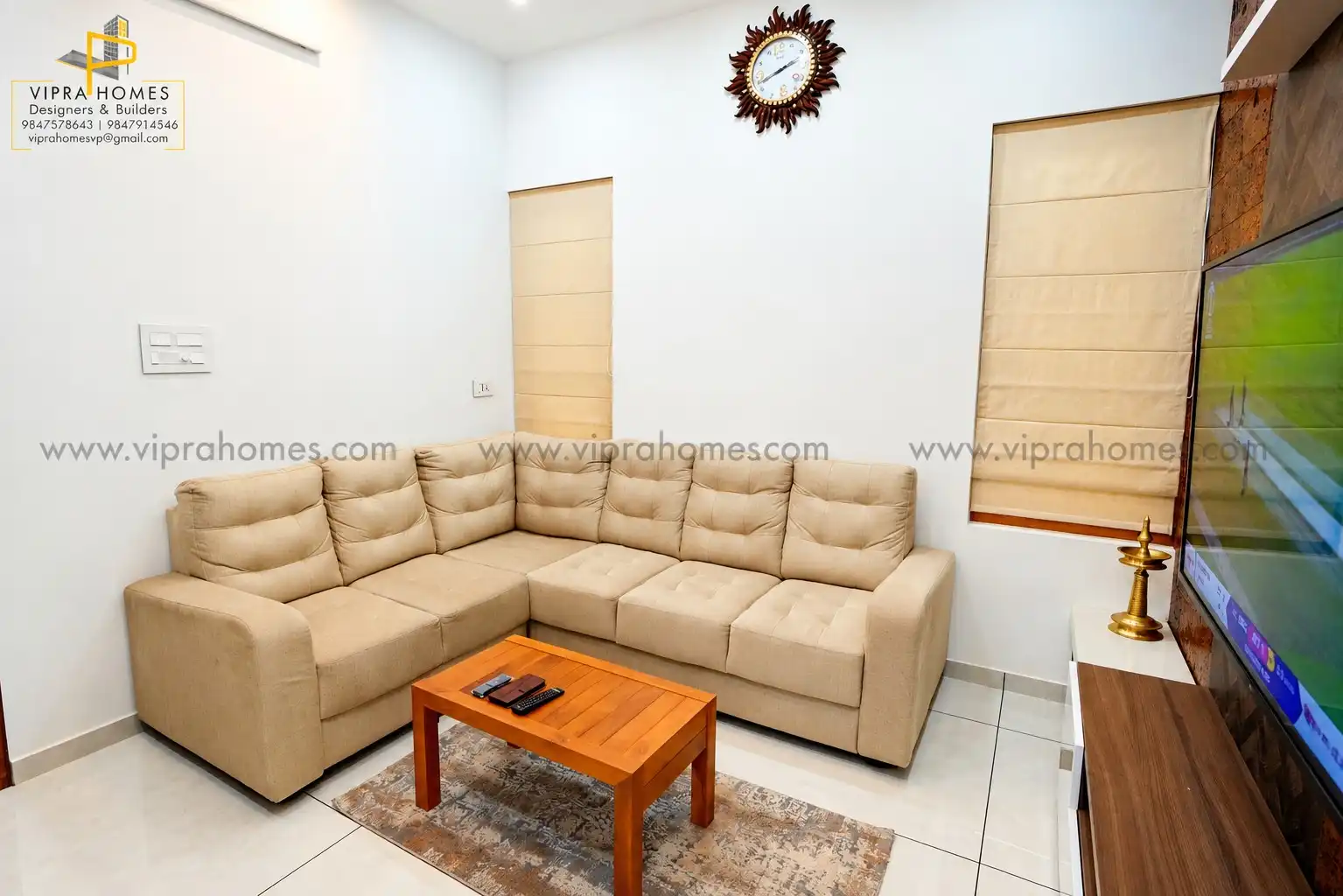 A living room by VIPRA HOMES with a beige L-shaped sofa, timber coffee table and Roman blinds