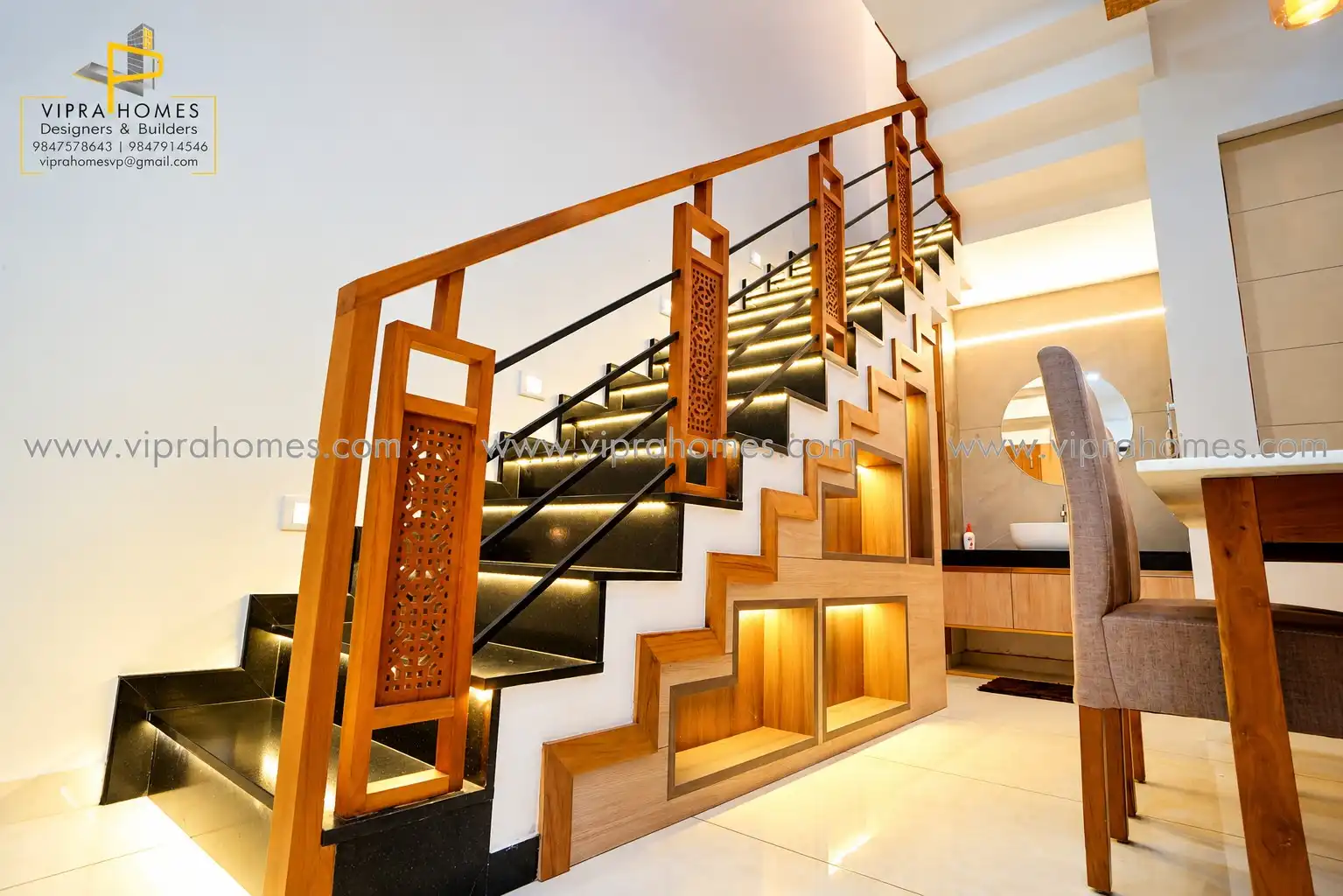 A staircase by VIPRA HOMES with carved timber balusters, black granite treads and lit display niches