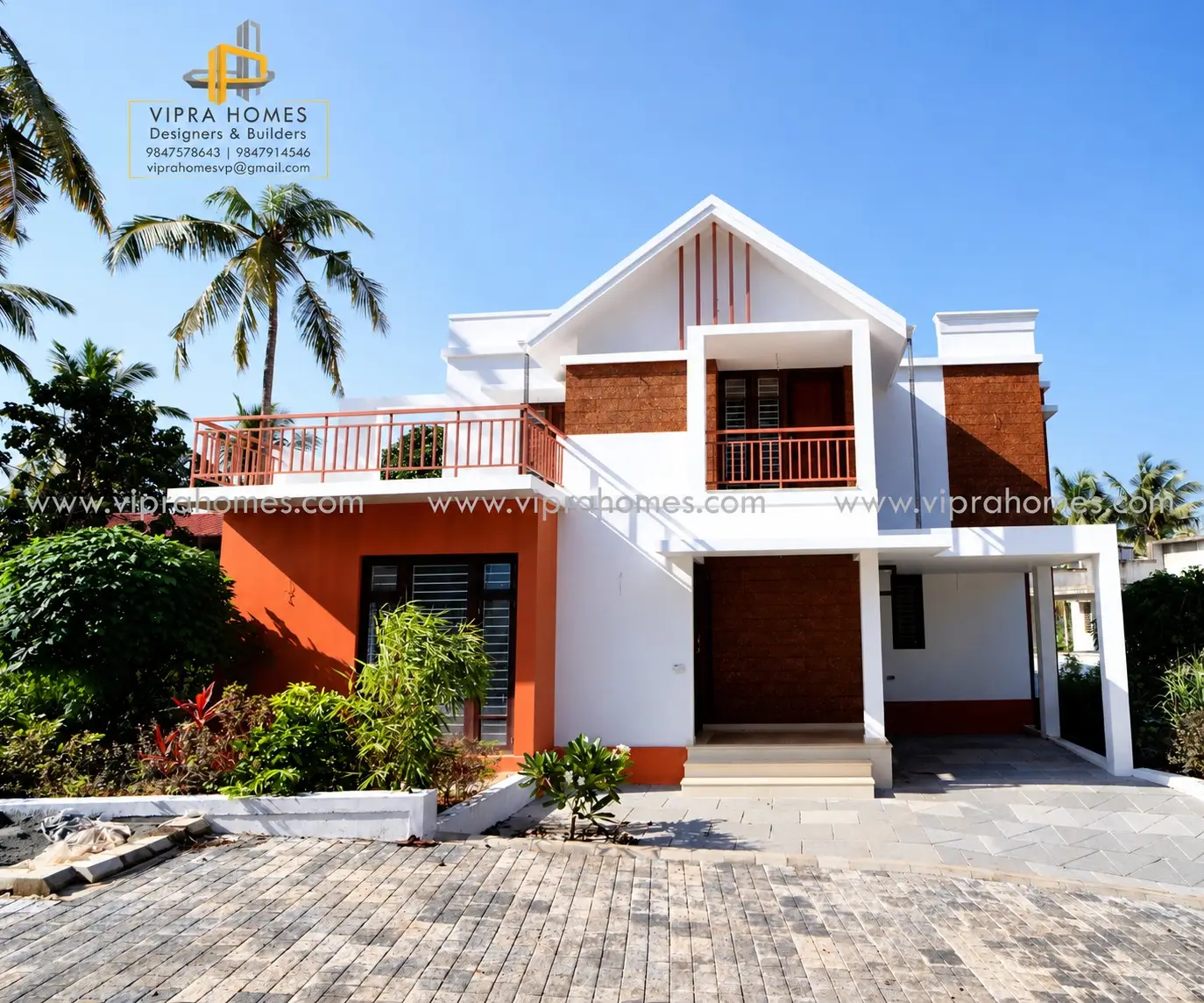 A two-storey home built by VIPRA HOMES, with a white facade, laterite-brick feature walls, a gabled roof and coconut palms against a clear sky